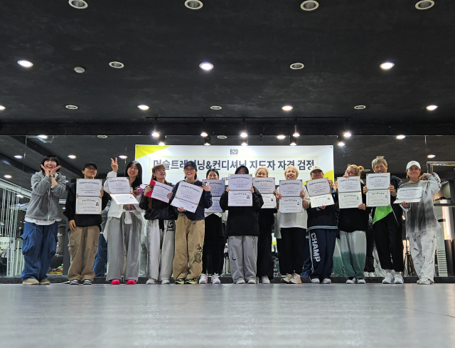 B2DTAINMENT가 운영하는 ‘머슬트레이닝&컨디셔닝 지도자 자격 검정’ 현장. 1기 교육생들이 교육 과정을 마치고 수료증을 수여받은 뒤 기념 촬영을 하고 있다. B2DTAINMENT는 2007년부터 토탈댄스지도자 자격 과정을 운영해왔으며, 2026년 머슬트레이닝&컨디셔닝 지도자 과정을 공식 론칭했다. 현장 중심 실습과 이론 교육을 병행하며 전문 지도자를 배출하고 있으며, 교육 수료 후 다양한 무대 및 현장 활동으로 연계되는 시스템을 구축하고