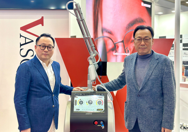 레이저옵텍 이창진 대표(오른쪽)와 아가파클리닉네트워크 최춘기 이사가 KIMES 현장에서 ‘바스큐라’를 배경으로 기념촬영을 하고 있다(사진=레이저옵텍)